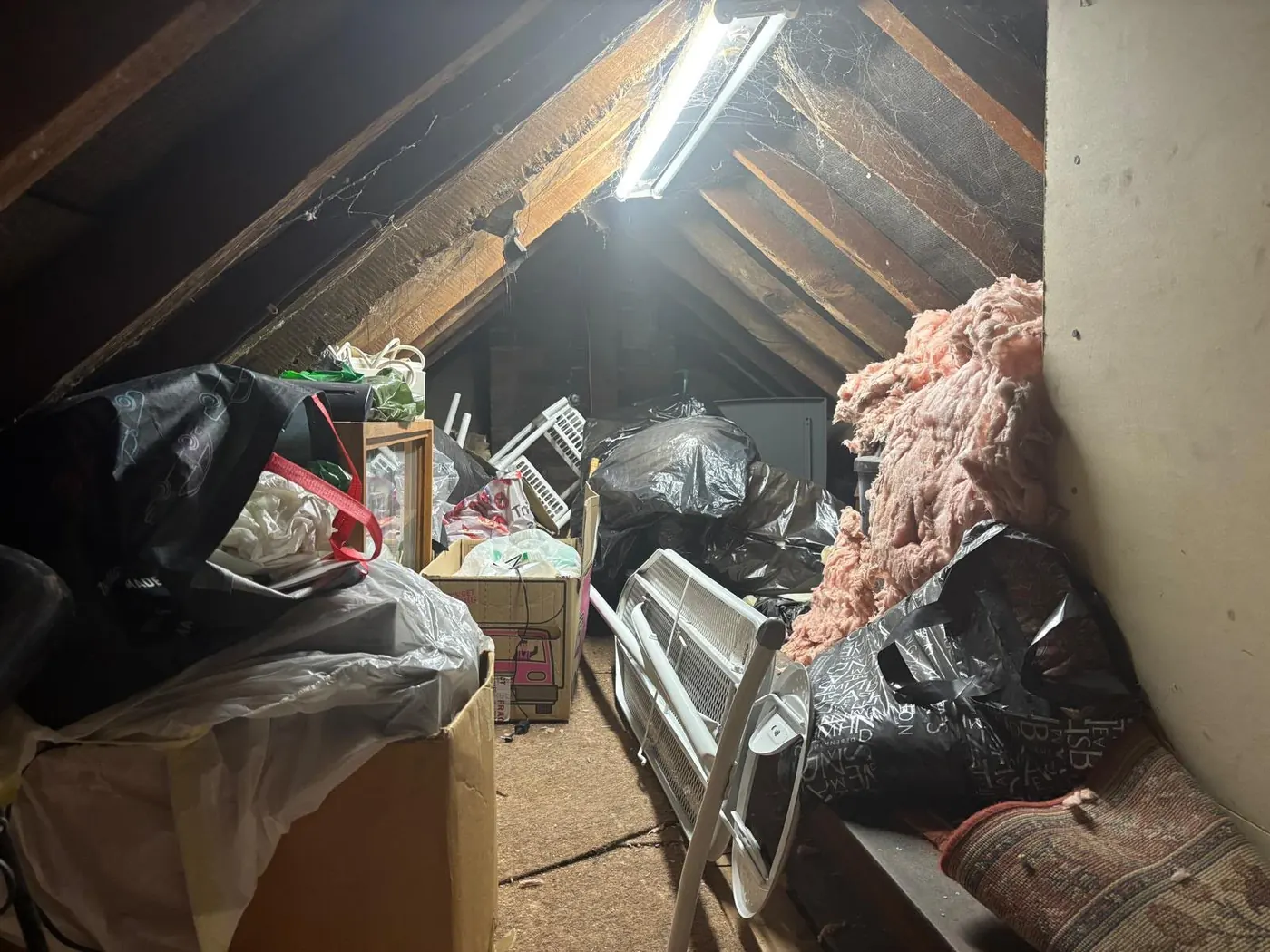 Dim attic space with stored bags, furniture and insulation ready for attic clearance