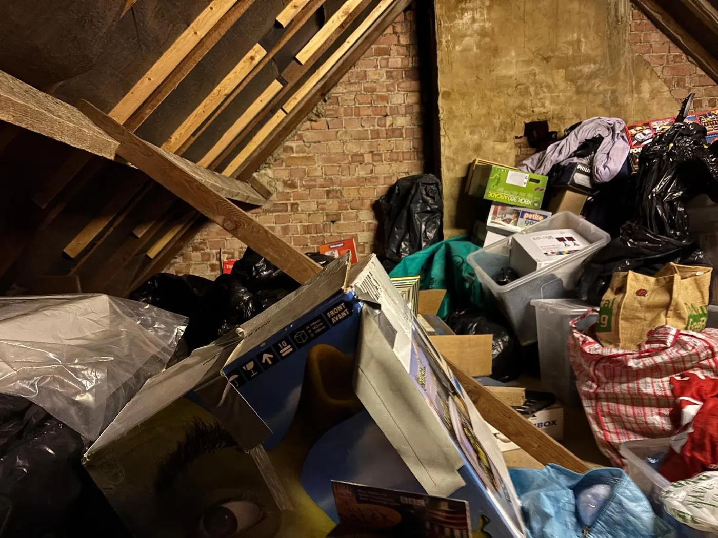 Cluttered loft with roof timbers, bags, boxes and old furniture awaiting loft clearance
