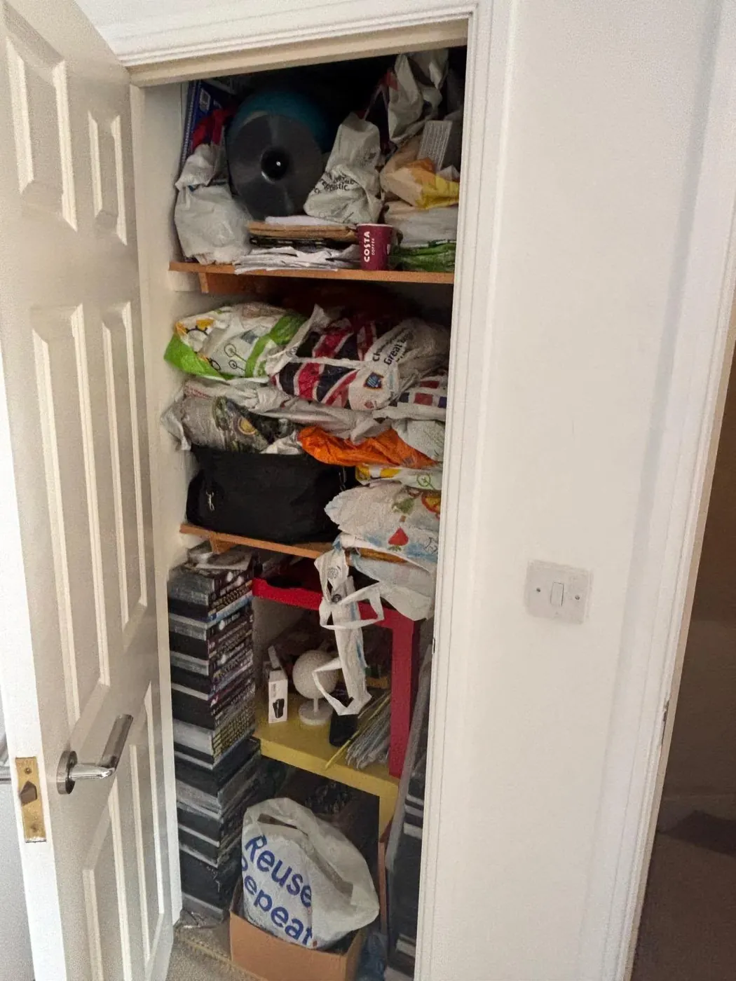 Overfilled cupboard with bags, books and household items during a clutter clearance